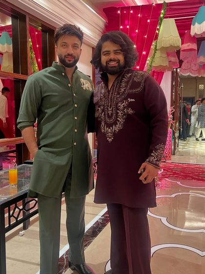 A custom olive green kurta set with an elephant motif, seen here at a wedding event. We also designed the guest's deep wine-colored kurta with intricate neck embroidery.