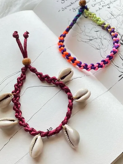 A pair of my beach-inspired anklets. One design features a deep red braided band adorned with natural cowrie shells for a classic beachy look, while the other is a vibrant, multi-colored braided anklet. Both are adjustable for a comfortable fit.
