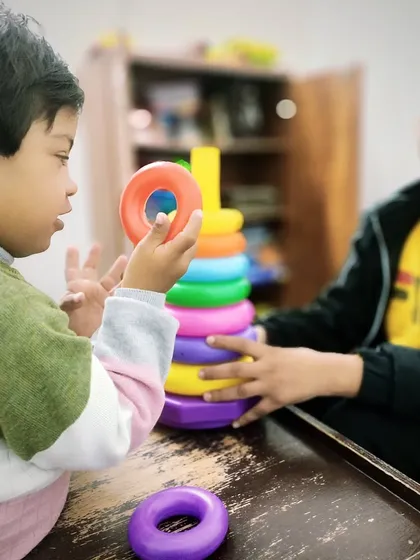 A child examines a colorful ring before placing it on the stack. This moment shows cognitive processing and motor planning, key elements we target in our occupational and speech therapy sessions.