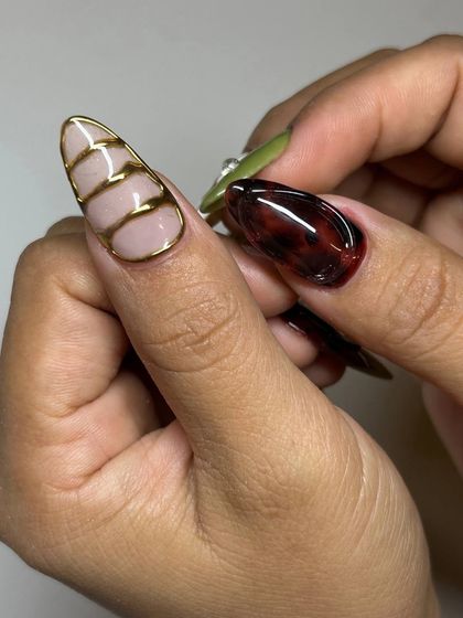 A close-up of the intricate details in this artistic set. One nail features a tortoise-shell effect, while another has delicate gold lines sculpted over a nude base.
