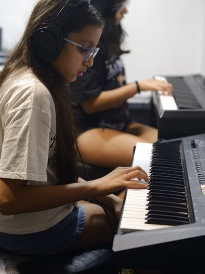 Two students practicing side by side on their own keyboards with headphones. This setup ensures everyone gets quality practice time.