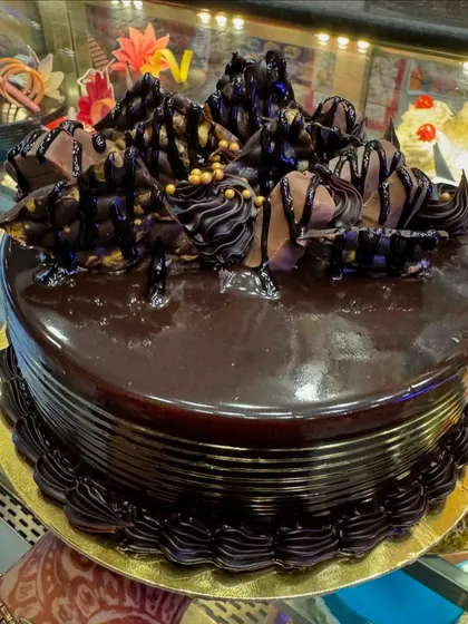 For the ultimate chocolate lover, I present our 5-star chocolate cake. It features a rich, moist chocolate sponge covered in a glossy chocolate ganache, with intricate piping and chocolate shard decorations. This is pure indulgence in every single bite.