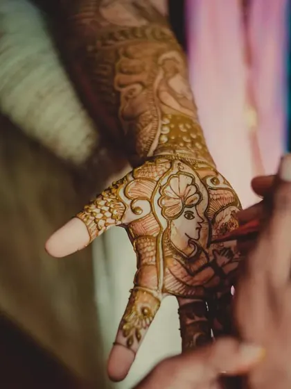 A detailed shot of intricate mehendi being applied, capturing the traditional art and anticipation of the wedding.