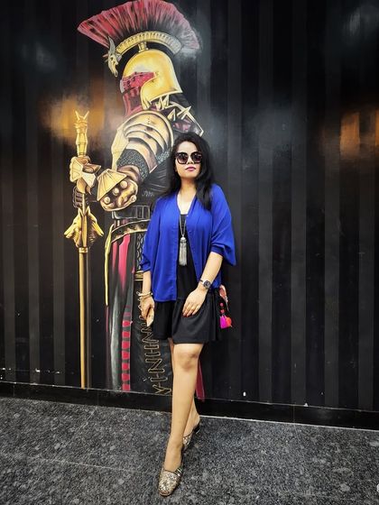 A black dress with a blue shrug and statement necklace, showing how to use color and accessories to create a unique look.