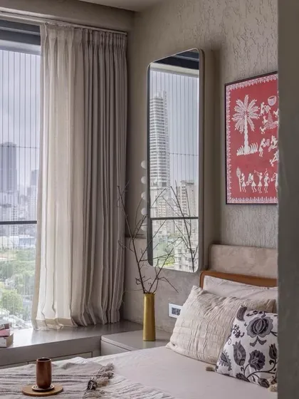 A bedroom with a view of the Mumbai skyline, where soft, neutral textiles and a piece of traditional Warli art create a space that is both urban and culturally rooted.