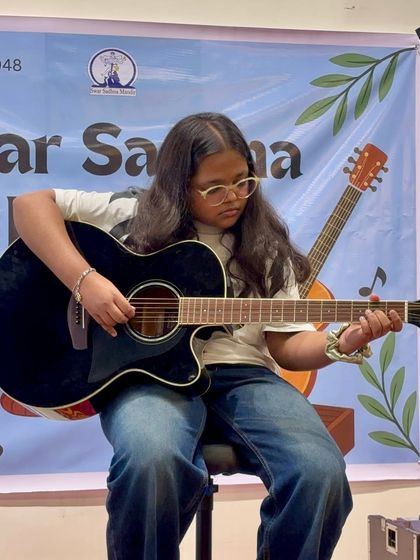 A young student confidently strums her guitar on stage. From the first lesson to the first performance, we guide our students every step of the way.