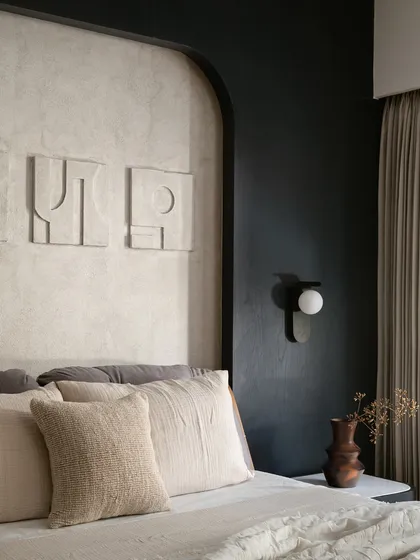 In this bedroom, I explored the power of a monochrome palette to create a space that is both youthful and sophisticated. The design is built on layers of texture, from the lime-washed wall behind the bed to the abstract art and soft linens. Every detail, including the modern wall sconce and custom headboard, was chosen to make the compact room feel intentional and full of character.