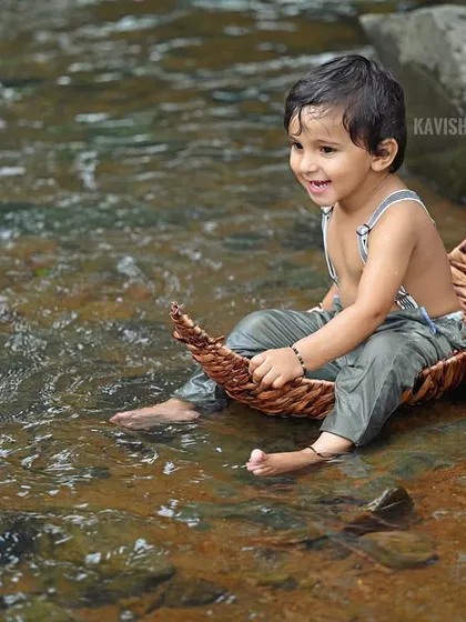 An adorable baby portrait taken by a stream, capturing a moment of playful splashing.