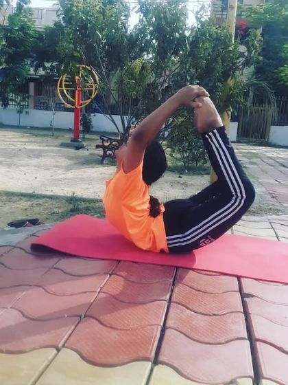 Holding Dhanurasana, or Bow Pose, in an outdoor park. This pose is excellent for strengthening the back muscles and opening up the entire front of the body.
