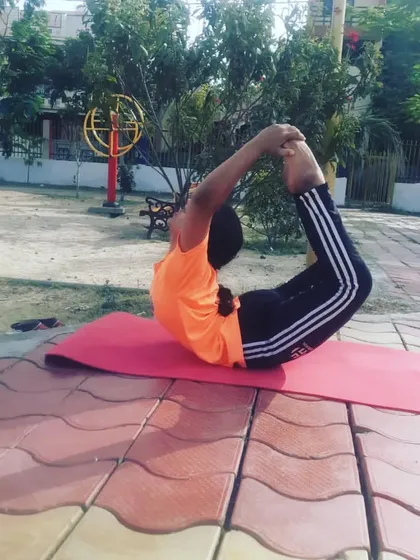 A deep Dhanurasana (Bow Pose) practiced on a tiled surface in a park. This pose strengthens the back muscles and improves posture by opening the chest and shoulders.