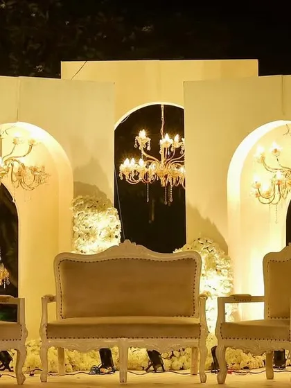 The reception stage, featuring elegant vintage furniture set against a backdrop of white arches and illuminated by beautiful chandeliers, creating a classic and timeless look.