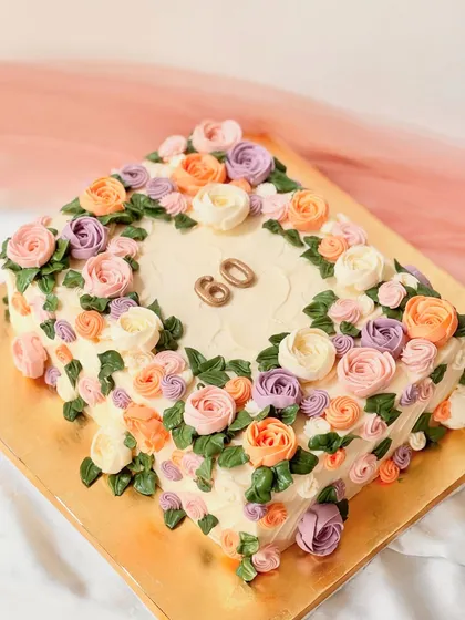 Celebrating a 60th birthday with a sophisticated square cake covered in a garden of hand-piped buttercream flowers. The pastel palette of peach, lavender, and pink creates a beautiful, classic floral design.