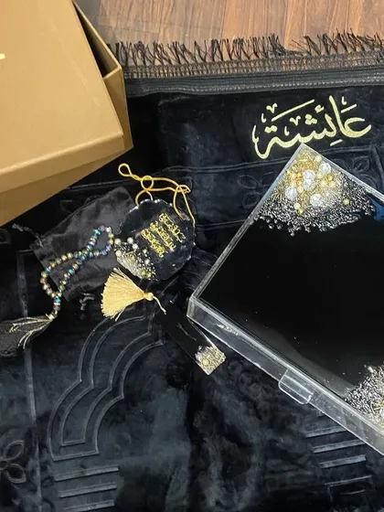 This luxurious black, gold, and silver combo set is a popular choice for a bridal gift. It includes a premium velvet prayer mat, a personalized acrylic Quran box, a resin Quran stand (rehal), a crystal tasbeeh, and a matching car hanging.