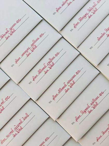 The neat, uniform lines of handwritten Gujarati calligraphy on a batch of wedding envelopes, ready to be sent out.