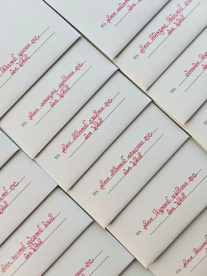 The neat, uniform lines of handwritten Gujarati calligraphy on a batch of wedding envelopes, ready to be sent out.