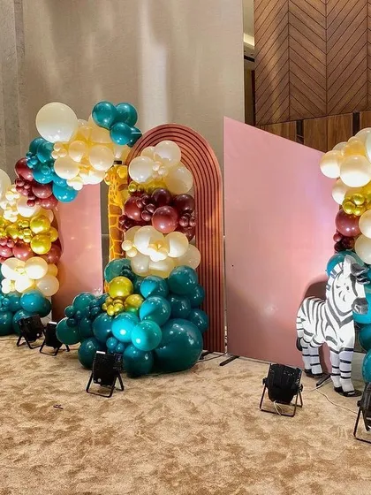 A stylish and modern take on the jungle theme, using a pink backdrop with arches, a zebra prop, and a unique color palette of teal, maroon, and gold balloons.