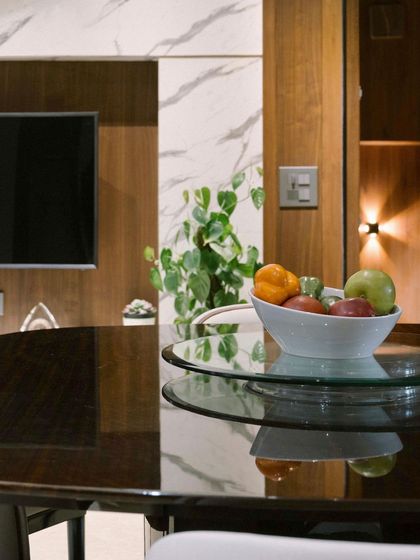 A view across a glossy dining table, where the reflection captures the wooden and marble-clad television wall in the background, showing the interplay of surfaces and materials.