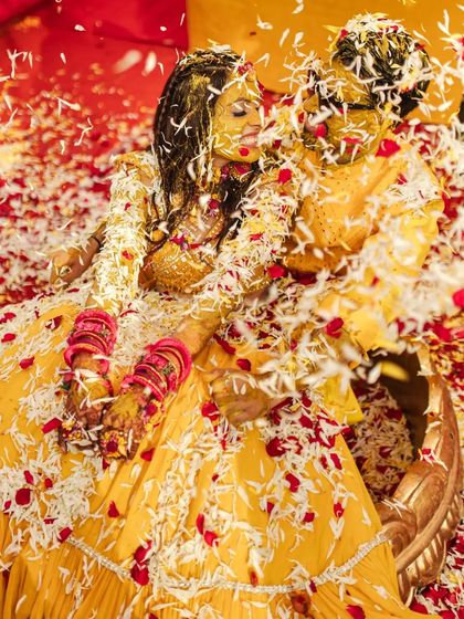 A stunning overhead shot of the couple covered in a sea of white and red petals, creating a dramatic and beautiful Haldi moment.