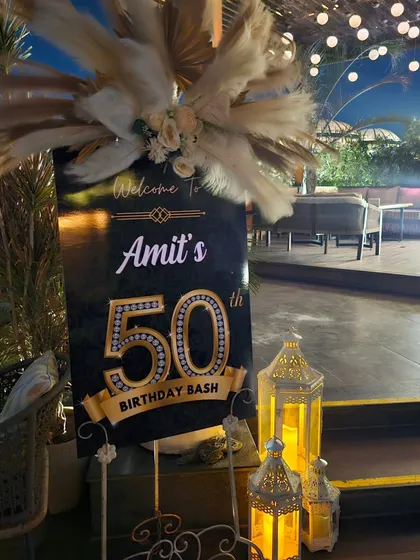 A close-up of the custom welcome sign for a 50th birthday bash. The sign features pampas grass, elegant fonts, and candle-lit lanterns for a warm and stylish welcome.