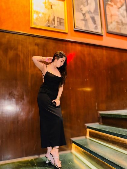 A moody, thoughtful pose in a black backless dress against a warm, wood-paneled wall.