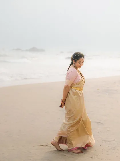 The bride walks along the shore, her expression serene and contemplative. This image has a beautiful, soft quality, capturing a moment of quiet solitude before the wedding festivities.