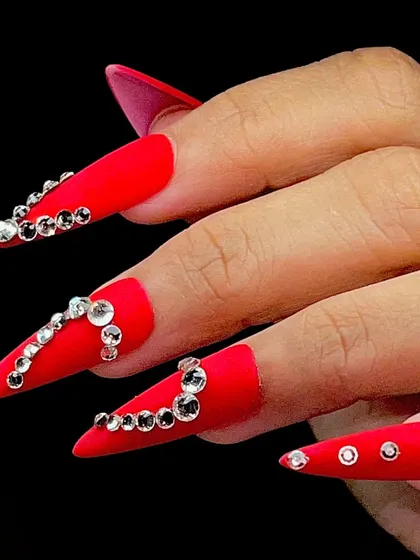 Fierce and glamorous. This set features long, stiletto-shaped matte red nails with intricate rhinestone placements.