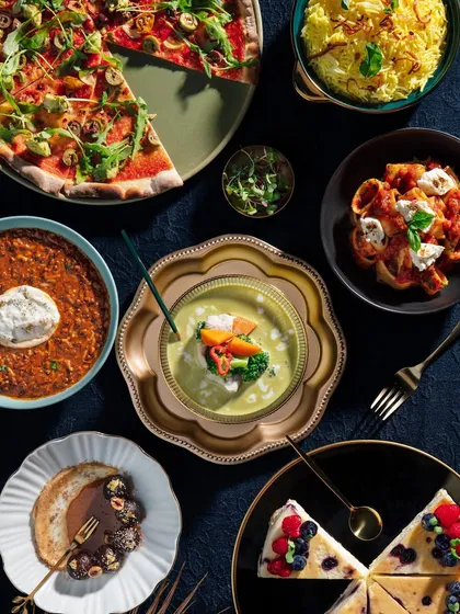 A full and abundant spread of dishes from Club Jolies, shot from above. This image is designed to look like a feast, showcasing everything from pizza and pasta to cheesecake, creating a drool-worthy visual.