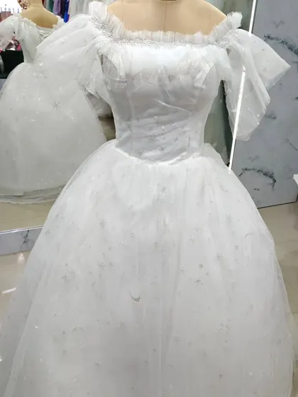 A classic fairytale bridal gown. This white off-shoulder ball gown is crafted from sparkling tulle and features romantic ruffled sleeves for a soft, dreamy look.