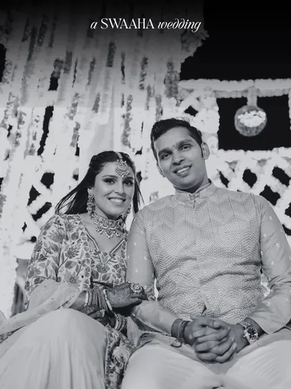 A classic black and white portrait of a couple at their Haldi ceremony, seated against a backdrop of hanging florals.