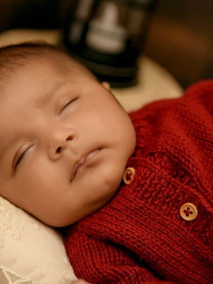 A detailed close-up of a sleeping baby in a cozy red knit sweater. This shot emphasizes the soft textures and the baby's peaceful state.
