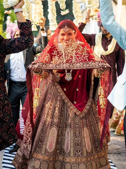 The bride's grand entrance under the phoolon ki chadar. Her magnificent velvet lehenga and radiant smile make for a breathtaking moment.