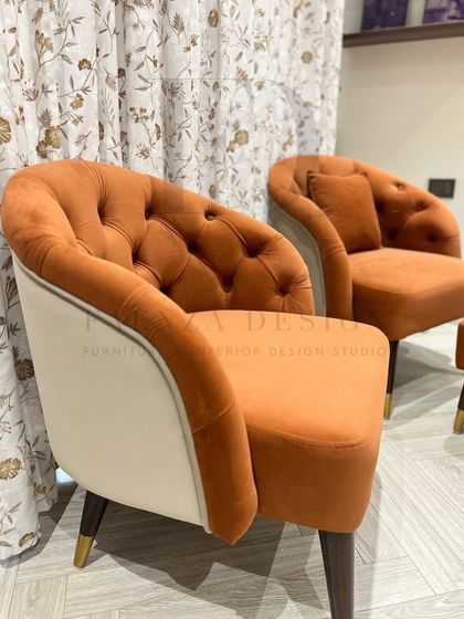 A set of two-tone accent chairs in a burnt orange velvet. The chairs feature a tufted back and a contrasting cream-colored exterior, creating a warm and inviting look.