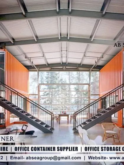 The interior of this multi-level container home reveals a spacious, open-plan design with a double-height ceiling and dramatic staircases. The original orange container walls are left exposed for an industrial-luxe feel.