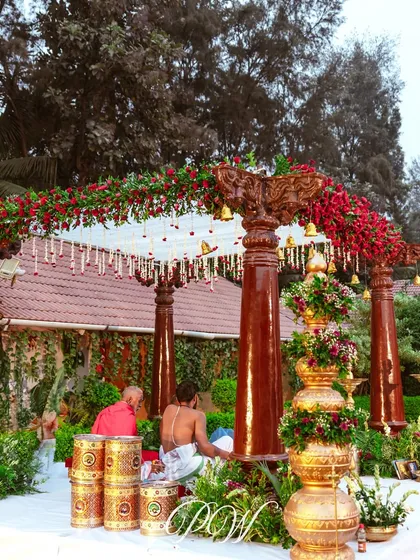 A classic South Indian wedding mandap with polished wooden pillars, a canopy of red roses, and traditional brass lamps. This setup is perfect for an intimate and authentic Muhurtham.