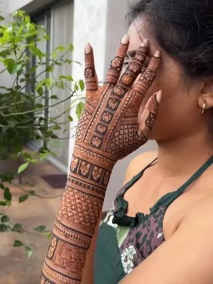 A lovely shot of a bride showing off her full-arm mehndi with a classic 'jaal' pattern and elephant border.