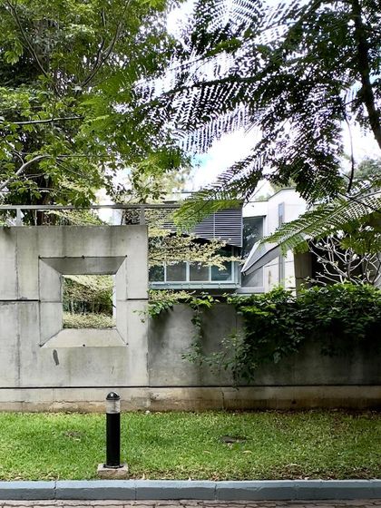 A view of the 'House of Stories' through an opening in its concrete boundary wall. The wall itself is a piece of architecture, framing views and creating a threshold between the public street and the private sanctuary within.