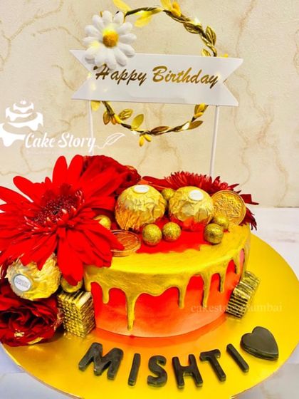 A vibrant red and gold drip cake. This design is loaded with Ferrero Rocher chocolates and red flowers, making it a rich and decadent choice for a celebration.
