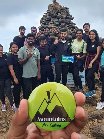 A guide holds up our badge at the Kumara Parvatha peak, with a small group of successful trekkers.