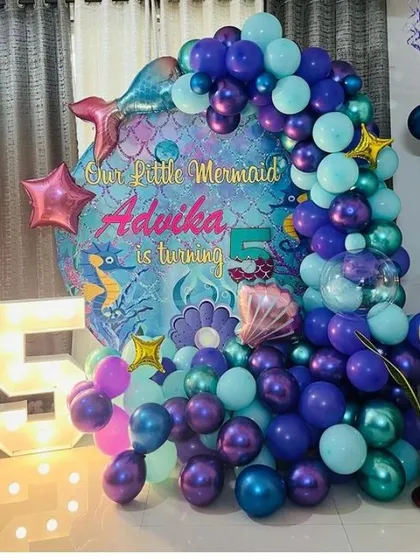 An enchanting "Our Little Mermaid" theme for a 5th birthday. This setup features a deep-sea-inspired balloon arch in shades of purple and teal, a custom backdrop, and a large light-up number '5' to make a splash.