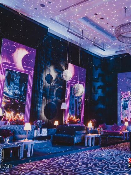 A wider view of the retro lounge area, showing multiple seating arrangements under hanging disco balls and moon-like orbs. The design uses large graphic backdrops and dramatic lighting to create a cohesive and immersive 80s theme.