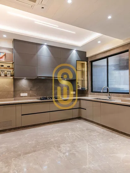 A complete view of a sleek, modern modular kitchen. This L-shaped layout maximizes space and functionality, featuring dual-tone cabinets, a built-in hob, and under-cabinet lighting for a bright and efficient cooking environment.