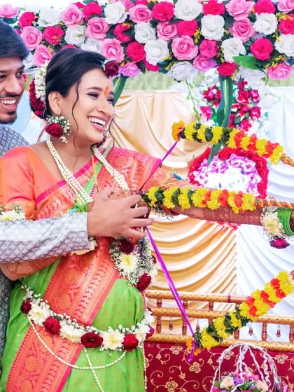 A playful moment from a traditional baby shower, with the couple holding a decorated bow and arrow, a common ritual in some cultures.
