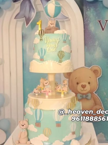 A close-up of a stunning two-tiered cake for a hot air balloon and teddy bear themed party. The cake is intricately decorated to match the sky-blue decor perfectly.
