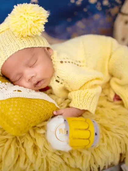 A close-up shot of a sleeping newborn in a yellow knit outfit, resting on a fuzzy yellow rug. This highlights the tiny, perfect features of a new baby.