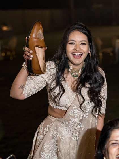 The 'brat bridesmaid' playfully holds up the groom's shoe during the 'joota chupai' ritual. Her embroidered lehenga is both beautiful and practical for participating in all the wedding fun.