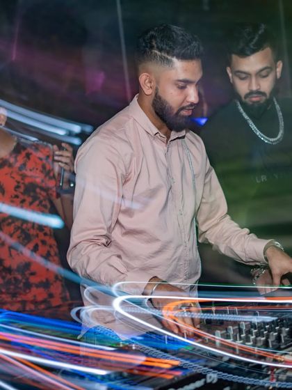 A long-exposure shot capturing the movement and energy around the DJ console. The light trails represent the fast-paced, dynamic nature of a live set.