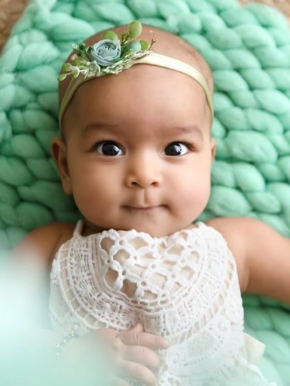 A close-up portrait of a baby girl looking directly at the camera with a sweet expression.