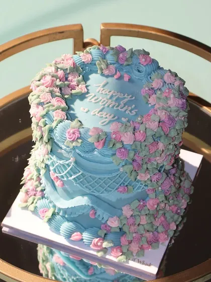 Celebrate the power and grace of women with our special Women's Day cake. This design features a cascade of pink and purple buttercream flowers over a blue cake.