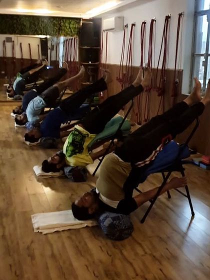 A class of students enjoying a supported inversion, Sarvangasana (Shoulderstand), using chairs and bolsters. This setup allows everyone to experience the calming benefits of the pose.