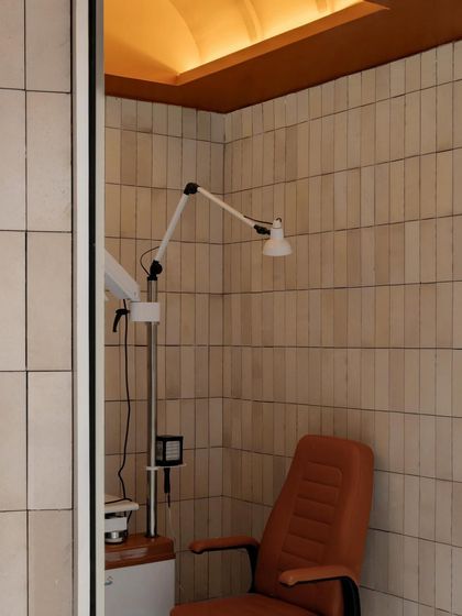 Even functional areas like the vision assessment room are designed with care, featuring the same warm material palette of neutral wall tiles and an arched ceiling to ensure a cohesive aesthetic throughout the store.